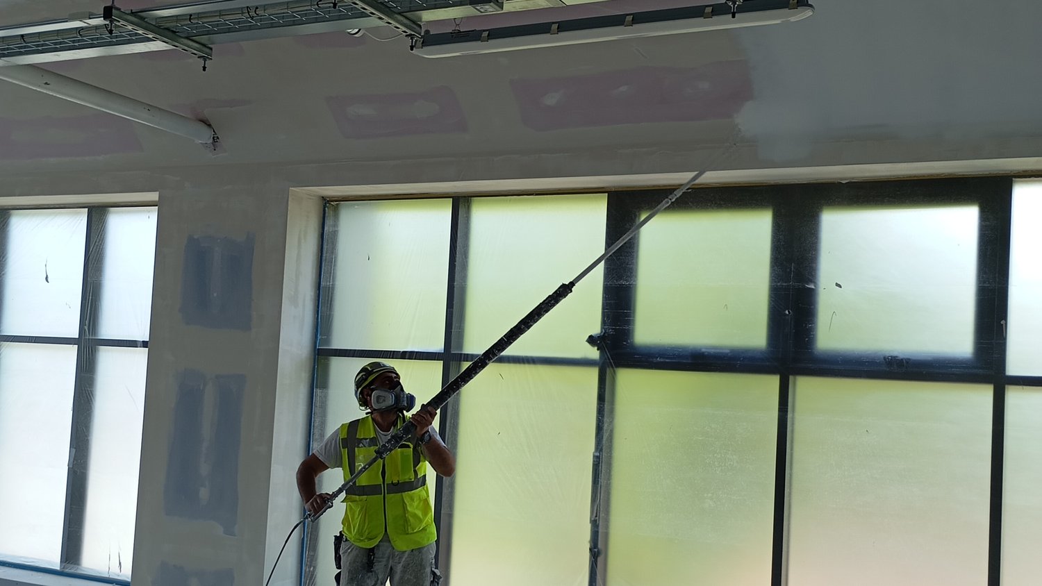 Operative airless spraying walls with an extension pole during a commercial fit-out, Crawley – Fixidea Coatings Ltd